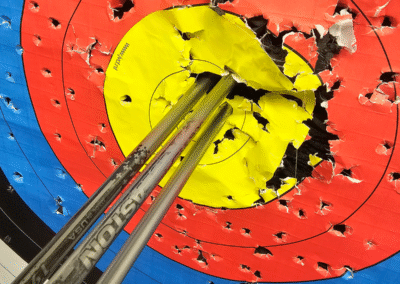 A close up of an archery target with 3 arrows fired into the central ring